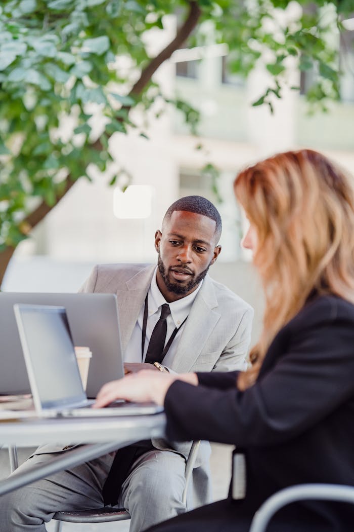 Businessman and businesswoman collaborating with laptops in an outdoor urban setting.